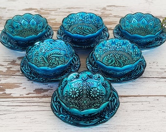 Puede incluir: Seis cuencos de cerámica turquesa con platillos a juego. Cada cuenco y platillo presenta un intrincado patrón floral y geométrico. Los cuencos tienen un borde festoneado y se asientan sobre una superficie de madera blanca.