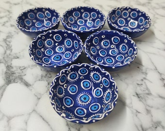 Może przedstawiać: Zestaw sześciu małych niebieskich miseczek ceramicznych z białymi i niebieskimi wzorami złego oka. Miski idealnie nadają się do serwowania małych przekąsek lub dipów.