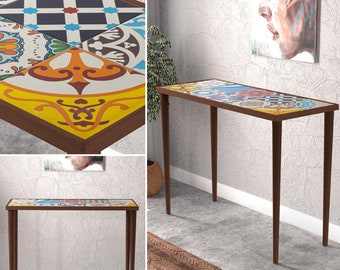May include: A brown console table with a colorful tile top. The table has a geometric pattern with shades of blue, yellow, orange, and green. The table is standing on a light gray floor with a brown rug.