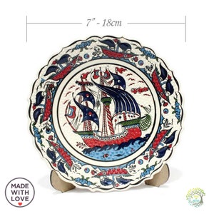 May include: A white ceramic decorative plate with a blue and red ship design. The plate is 7 inches in diameter and has a scalloped edge.
