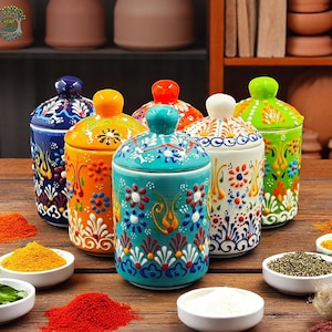 以下が含まれることがあります： 蓋付きのカラフルなセラミック製スパイスジャー6個。ジャーは青、緑、オレンジ、白の複雑な花柄で飾られています。ジャーは木製の表面に一列に並べてあります。