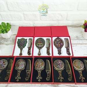 May include: Ornate antique-style mirror and comb sets in red gift boxes. The mirrors and combs have intricate designs with colorful jewel accents. The sets are displayed on a white brick background.