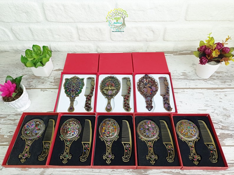 May include: Ornate antique-style mirror and comb sets in red gift boxes. The mirrors and combs have intricate designs with colorful jewel accents. The sets are displayed on a white brick background.