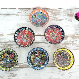 Puede incluir: Conjunto de seis cuencos peque&ntilde;os y redondos de cer&aacute;mica con intrincados patrones florales coloridos. Cada cuenco presenta un dise&ntilde;o &uacute;nico con una variedad de colores, incluyendo rojo, azul, verde y amarillo. Los cuencos est&aacute;n dispuestos sobre una superficie de madera blanca envejecida.