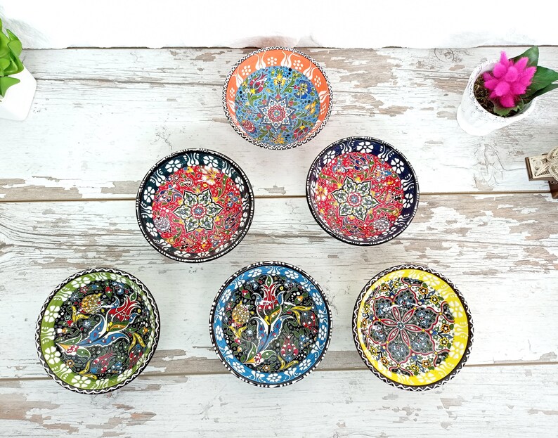 Puede incluir: Conjunto de seis cuencos peque&ntilde;os y redondos de cer&aacute;mica con intrincados patrones florales coloridos. Cada cuenco presenta un dise&ntilde;o &uacute;nico con una variedad de colores, incluyendo rojo, azul, verde y amarillo. Los cuencos est&aacute;n dispuestos sobre una superficie de madera blanca envejecida.