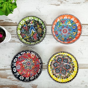 Puede incluir: Cuatro cuencos decorativos de cer&aacute;mica con intrincados dise&ntilde;os florales. Los cuencos presentan una variedad de colores, incluyendo verde, rojo, azul, naranja y amarillo. Cada cuenco tiene un dise&ntilde;o &uacute;nico, con patrones y bordes detallados. Los cuencos est&aacute;n dispuestos sobre una superficie de madera blanca.