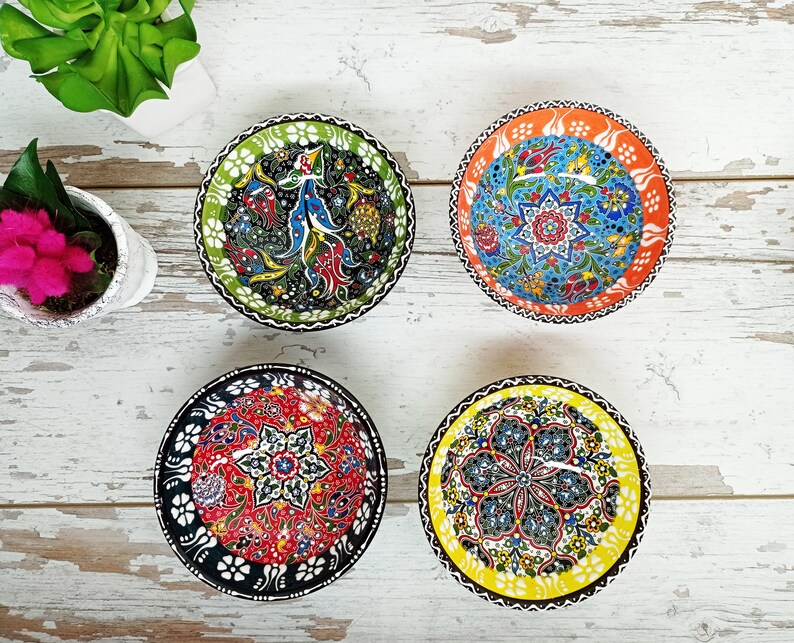 Puede incluir: Cuatro cuencos decorativos de cer&aacute;mica con intrincados dise&ntilde;os florales. Los cuencos presentan una variedad de colores, incluyendo verde, rojo, azul, naranja y amarillo. Cada cuenco tiene un dise&ntilde;o &uacute;nico, con patrones y bordes detallados. Los cuencos est&aacute;n dispuestos sobre una superficie de madera blanca.