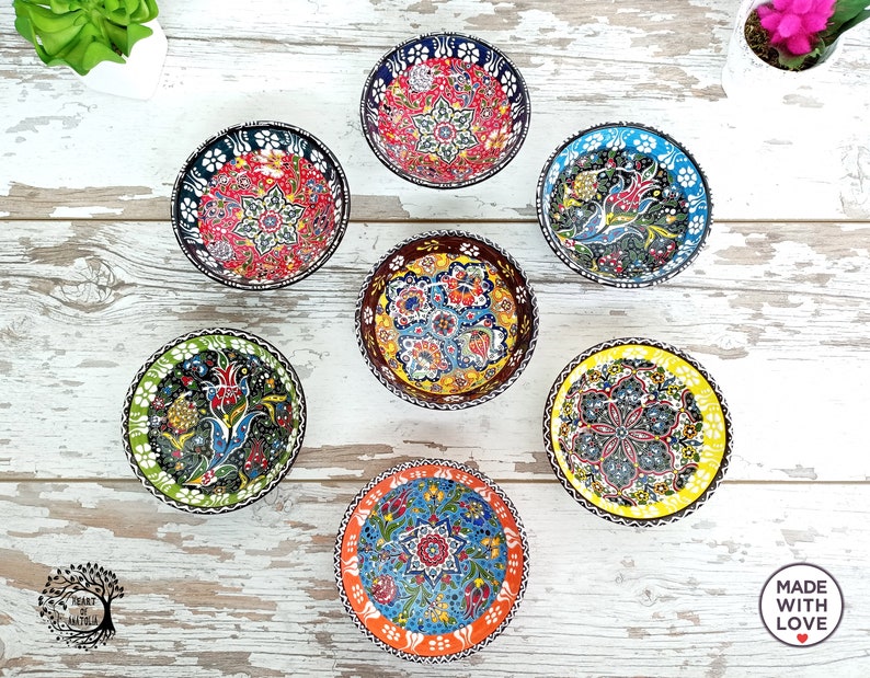 Puede incluir: Una colecci&oacute;n de siete cuencos peque&ntilde;os y redondos de cer&aacute;mica con intrincados y coloridos dise&ntilde;os florales. Cada cuenco presenta un dise&ntilde;o &uacute;nico con una variedad de colores, incluyendo rojo, azul, amarillo y verde. Los cuencos est&aacute;n dispuestos sobre una superficie de madera clara.