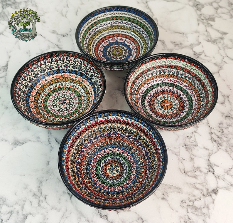 May include: Four ceramic bowls with intricate, colorful patterns. Each bowl features a black rim and a detailed design in shades of blue, orange, green, and red. The bowls are arranged in a square formation, showcasing their decorative appeal.