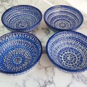 May include: Four blue ceramic bowls with intricate white and blue floral patterns. The bowls are arranged in a square, showcasing their detailed designs. The bowls are likely for serving food.