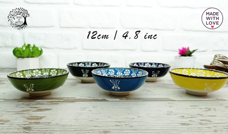 Puede incluir: Una colecci&oacute;n de cinco cuencos de cer&aacute;mica, cada uno de 12 cm de di&aacute;metro, con base blanca y dise&ntilde;os coloridos. Los cuencos son verdes, negros, azules y amarillos, con motivos florales. El texto "12cm / 4.8 inc" es visible.