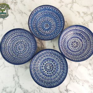 May include: Four blue and white ceramic plates with intricate, symmetrical patterns. The plates have a dark blue rim and a detailed, floral-like design in shades of blue and white. The plates are arranged on a white and gray marble surface.