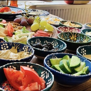 May include: A table laden with a variety of breakfast foods. Several small, decorative bowls filled with olives, sliced cucumbers, tomatoes, and dips. Other plates hold cheese, fruit, and nuts. The bowls have a blue and white floral design.