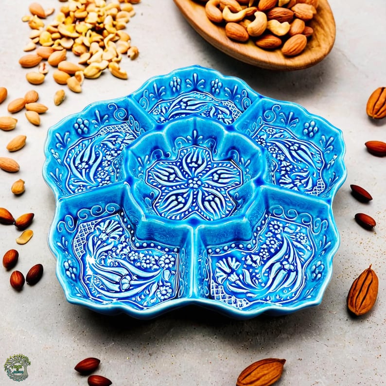 May include: A turquoise ceramic serving dish with a floral design, divided into six sections. The dish is surrounded by almonds, cashews, and other nuts.