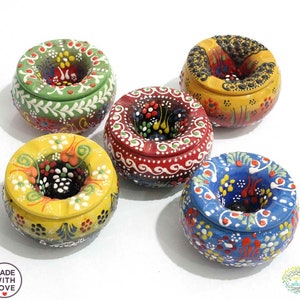 Può includere: Cinque posacenere in ceramica colorati con intricati disegni floreali. Ogni posacenere ha una forma rotonda con un foro centrale per le sigarette. I posacenere sono dipinti in tonalità di verde, giallo, rosso, blu e nero.