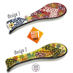 May include: Two ceramic spoon rests with colorful floral designs. Design 1 features red, white, and blue patterns, while Design 2 showcases yellow, green, and red motifs. The spoon rests have a black border and are labeled "Design 1" and "Design 2".