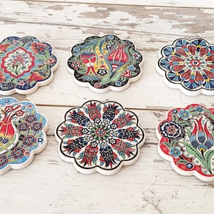 Puede incluir: Seis posavasos decorativos de cer&aacute;mica con dise&ntilde;os florales en rojo, azul, verde y amarillo. Cada posavasos tiene un borde festoneado y un dise&ntilde;o &uacute;nico. Est&aacute;n dispuestos sobre una superficie de madera blanca envejecida. La frase "MADE WITH LOVE" es visible.