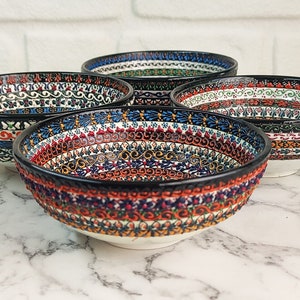 May include: Four ceramic bowls with intricate, colorful patterns. The bowls feature a black rim and a white base. The patterns include floral and geometric designs in red, blue, green, and orange. The bowls are arranged on a marble surface.