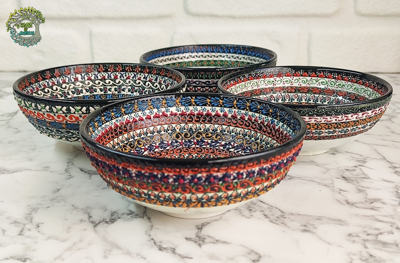 May include: Four ceramic bowls with intricate, colorful patterns. The bowls feature a black rim and a white base. The patterns include floral and geometric designs in red, blue, green, and orange. The bowls are arranged on a marble surface.