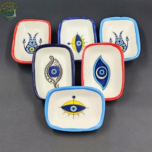 May include: Six small white ceramic dishes with blue and yellow evil eye designs. The dishes are perfect for serving small snacks or dips.