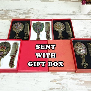 May include: Ornate antique-style mirror and comb sets in red gift boxes. The mirrors and combs have intricate designs with colorful jewel accents. The text "SENT WITH GIFT BOX" is displayed.