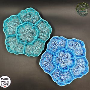 May include: Two ceramic serving platters in shades of blue. The platters have a floral design with a central flower and surrounding compartments. The platters are decorated with white floral patterns. The text "MADE WITH LOVE" is visible.