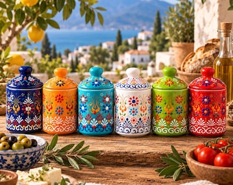 May include: A set of six cylindrical ceramic jars with lids, each featuring a vibrant, multi-colored floral pattern. The jars are arranged in a row on a wooden surface, displaying colors including dark blue, orange, turquoise, white, green, and red.