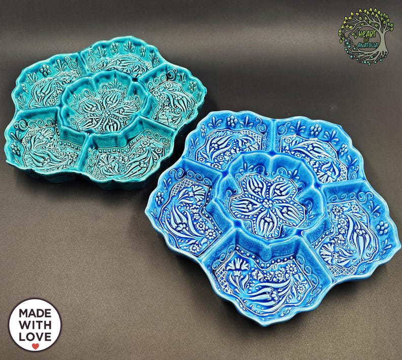 May include: Two ceramic serving platters in shades of blue, featuring a floral design. Each platter has a central compartment surrounded by six smaller sections. The platters are decorated with white floral patterns and have a scalloped edge.