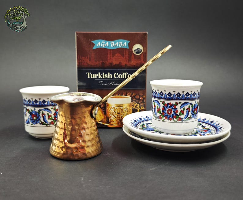 May include: A hammered copper coffee pot with a long handle, two white ceramic cups with blue, red, and green floral patterns, two matching saucers, and a brown box labeled AĞA BABA Turkish Coffee with an image of a coffee cup on the front.