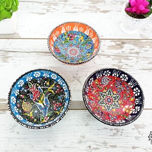 Puede incluir: Tres cuencos decorativos de cer&aacute;mica con intrincados dise&ntilde;os florales. Los cuencos presentan colores vibrantes como el rojo, el azul, el naranja y el verde. Cada cuenco tiene un dise&ntilde;o &uacute;nico, con patrones detallados sobre un fondo negro o blanco. Los cuencos est&aacute;n sobre una superficie de madera blanca.