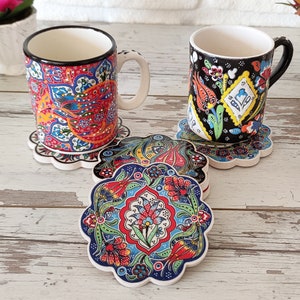 Puede incluir: Dos tazas de cer&aacute;mica con intrincados y coloridos dise&ntilde;os florales descansan sobre posavasos a juego. Los posavasos y las tazas presentan una vibrante mezcla de dise&ntilde;os rojos, azules, amarillos y verdes. Las tazas tienen bordes y asas negros, y los posavasos tienen un borde festoneado.