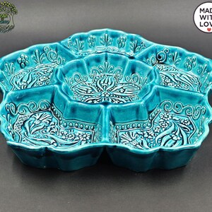 May include: A turquoise ceramic serving dish with multiple compartments. The dish has a scalloped edge and is decorated with floral and scroll patterns. The words "MADE WITH LOVE" are in a white circle on the upper right.