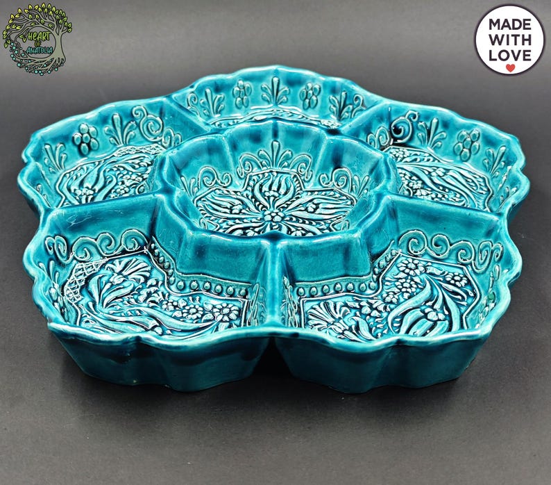 May include: A turquoise ceramic serving dish with multiple compartments. The dish has a scalloped edge and is decorated with floral and scroll patterns. The words "MADE WITH LOVE" are in a white circle on the upper right.