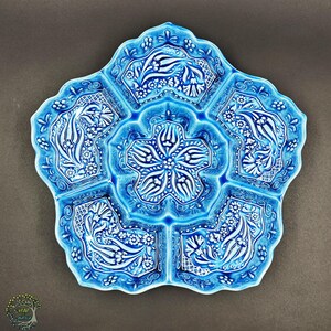 May include: A turquoise ceramic serving dish with a floral design. The dish is shaped like a flower with five sections and a central compartment. The raised white floral pattern adds a decorative touch to the serving dish.