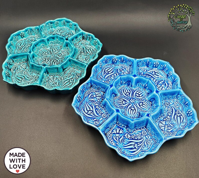 May include: Two ceramic serving platters in shades of blue and turquoise. Each platter has a central compartment surrounded by six smaller sections. The platters feature a floral and leaf design in white relief. The platters are handmade and labeled "MADE WITH LOVE".