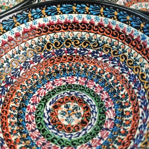 May include: Close-up of several ceramic bowls with intricate, colorful patterns. The bowls feature concentric circles of detailed designs in shades of blue, orange, green, and red. The rims are black, and the overall aesthetic is decorative and artisanal.