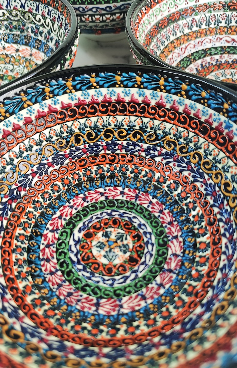 May include: Close-up of several ceramic bowls with intricate, colorful patterns. The bowls feature concentric circles of detailed designs in shades of blue, orange, green, and red. The rims are black, and the overall aesthetic is decorative and artisanal.