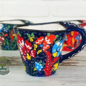 Może przedstawiać: Zestaw trzech niebieskich i białych ceramicznych filiżanek do kawy z kolorowymi wzorami kwiatowymi. Filiżanki mają unikalny kształt z szeroką podstawą i wąskim wierzchołkiem.