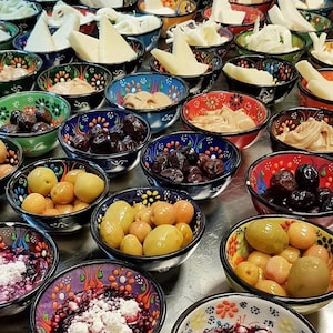 May include: A collection of small, decorative bowls filled with various foods. The bowls have colorful floral patterns and contain items like olives, cheeses, and spreads. The arrangement suggests a buffet or a selection of appetizers.