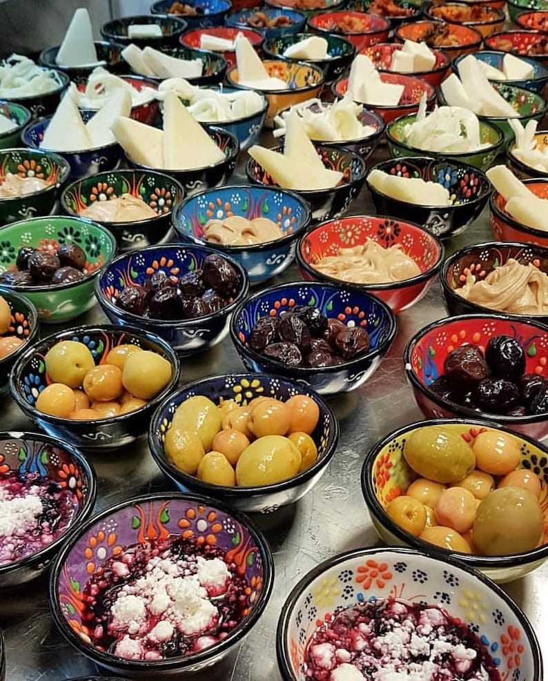 May include: A collection of small, decorative bowls filled with various foods. The bowls have colorful floral patterns and contain items like olives, cheeses, and spreads. The arrangement suggests a buffet or a selection of appetizers.
