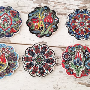 Puede incluir: Seis posavasos de cer&aacute;mica con dise&ntilde;os florales en rojo, azul, verde y amarillo. Cada posavasos tiene un dise&ntilde;o &uacute;nico y un borde festoneado. Dispuestos sobre una superficie de madera blanca.