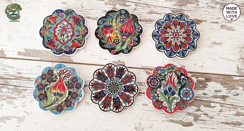 Puede incluir: Seis posavasos de cer&aacute;mica con dise&ntilde;os florales en rojo, azul, verde y amarillo. Cada posavasos tiene un dise&ntilde;o &uacute;nico y un borde festoneado. Dispuestos sobre una superficie de madera blanca.
