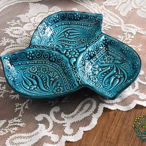 May include: A turquoise blue ceramic serving dish with three sections. The dish is decorated with intricate floral patterns and swirls.