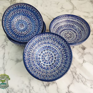 May include: A set of five ceramic bowls with a deep blue and white floral pattern. The bowls have a circular design with intricate details. The bowls are arranged on a marble surface.