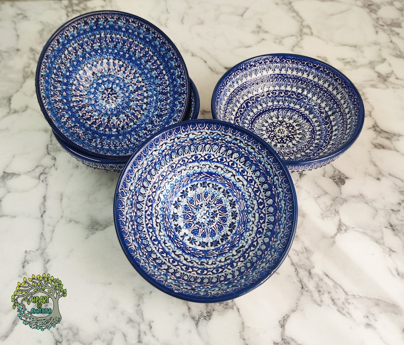 May include: A set of five ceramic bowls with a deep blue and white floral pattern. The bowls have a circular design with intricate details. The bowls are arranged on a marble surface.