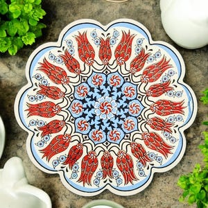 Puede incluir: Un posavasos de cerámica blanca con un diseño floral azul y rojo. El diseño presenta tulipanes rojos y flores azules en un patrón circular.