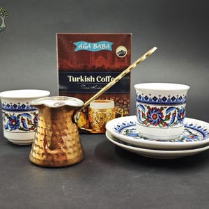 May include: A hammered copper coffee pot with a long handle, two white ceramic cups with blue, red, and green floral patterns, two matching saucers, and a brown box labeled AĞA BABA Turkish Coffee with an image of a coffee cup on the front.
