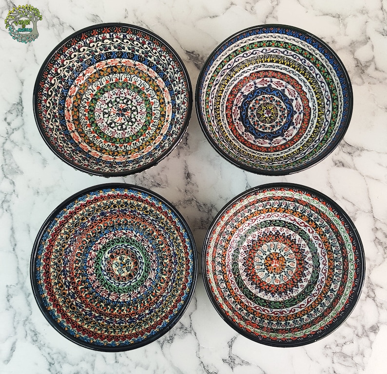 May include: Four decorative ceramic bowls with intricate, colorful patterns. Each bowl features a black rim and a unique design with concentric circles of red, blue, green, and orange. The bowls are arranged on a white marble surface.