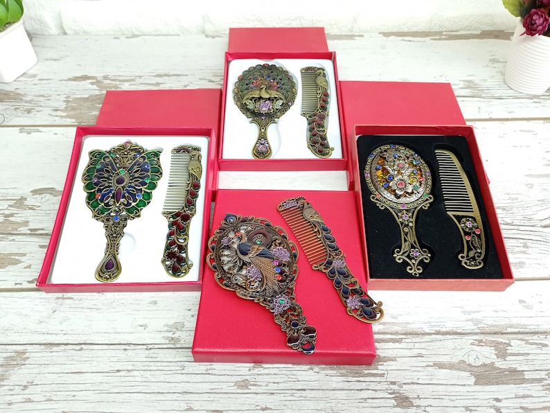May include: Ornate antique-style mirror and comb sets in red gift boxes. The sets feature detailed metalwork with colorful jewel accents. The mirrors and combs have a peacock or floral design.