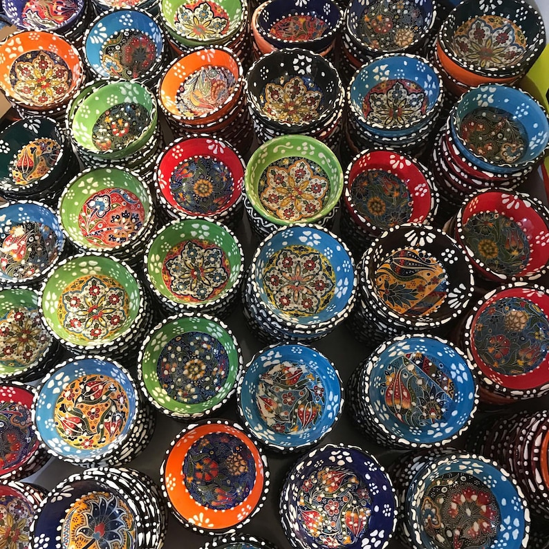 May include: A collection of colorful ceramic bowls with intricate floral and geometric patterns. The bowls are stacked, showcasing a variety of colors including blue, green, red, orange, and black. Each bowl features a unique design, creating a vibrant display.